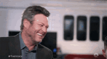 a man in a suit is laughing with the hashtag #thevoice on the bottom