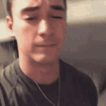 a man wearing a black shirt and a necklace is making a sad face .