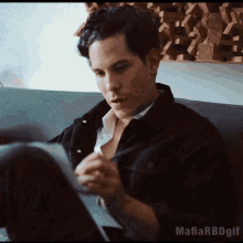 a man in a black jacket is sitting on a couch looking at a piece of paper ..