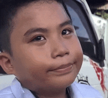 a young boy is smiling and looking at the camera while standing in front of a white truck .