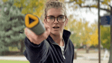 a woman wearing glasses is pointing at something with a yellow triangle in the middle
