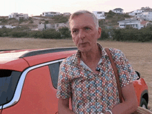 a man wearing a colorful shirt is standing in front of an orange car