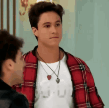 a young man wearing a plaid jacket and a necklace is standing next to another young man .