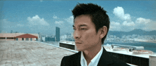 a man in a suit and white shirt is standing on a rooftop overlooking a city