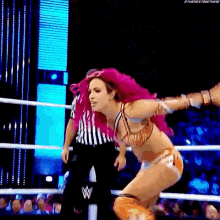 a woman with pink hair is jumping in the air in a wrestling ring .