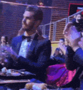 a man in a tuxedo and bow tie is sitting at a table with a plate of food .