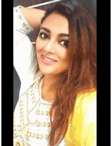 a woman wearing a white shirt and a yellow jacket smiles for the camera