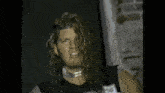 a man with long hair is wearing a choker and a black shirt .