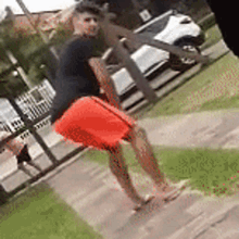 a man in orange shorts is standing on a sidewalk next to a car .