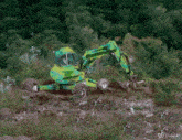 a green excavator is driving through a lush green forest on a hillside