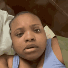 a woman in a blue tank top is laying on a bed and making a funny face
