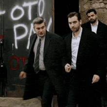 three men in suits are walking in front of a wall that says oto pa