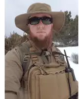 a bearded man wearing a hat and sunglasses stands in the snow