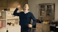 a man in a blue sweater is standing in front of a cabinet