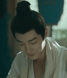 a man with a bun on his head is wearing a white robe