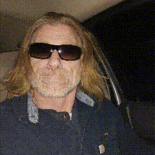 a man with long hair and sunglasses is sitting in a car