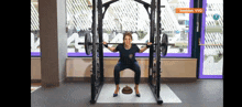 a woman squatting in front of a barbell in a gym with a sign that says beelden vvd on it