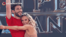 a man in a red shirt is hugging a woman in front of a sign that says eltrecetv.com