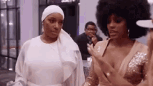 two women are standing next to each other in a room and talking .