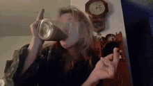a woman is drinking from a bottle in front of a wall clock that shows the time as 2:30