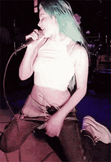 a woman with green hair is singing into a microphone while kneeling down .