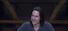 a man with long hair and a gray shirt smiles