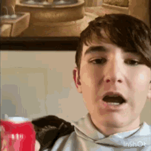 a young man is holding a red can of soda in front of a picture .
