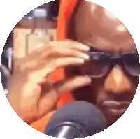 a man wearing sunglasses and an orange shirt is talking into a microphone