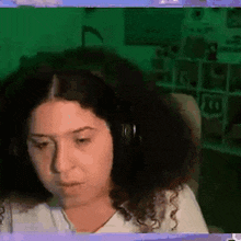 a woman with curly hair wearing headphones is sitting in front of a green screen .