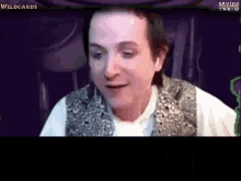 a man in a vest is smiling in front of a screen that says wildcards .