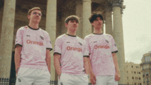 three boys wearing pink shirts that say orange are standing in front of a building
