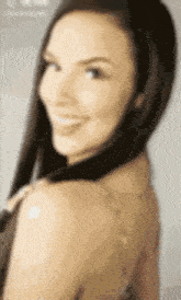 a woman with long dark hair is smiling and looking over her shoulder .