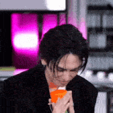 a man in a black jacket is holding an orange cup in his hands .
