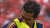 a man with curly hair is wearing a yellow vest and covering his face with his hand .