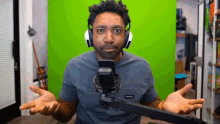 a man wearing headphones is sitting in front of a green screen and talking into a microphone .