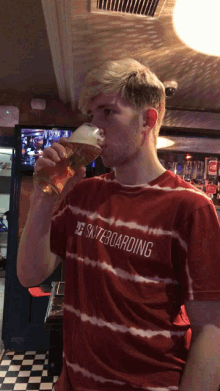 a man wearing a red shirt that says skateboarding is drinking a glass of beer