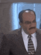 a bald man with a mustache wearing a suit and tie making a funny face
