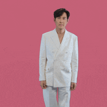 a man in a white suit is standing on a pink background