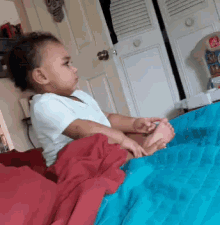 a baby is sitting on a bed with a blue blanket and a red blanket