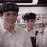 two young men wearing hats and aprons are smiling in a kitchen