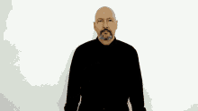 a bald man with a beard is wearing a black shirt and making a gesture with his hands .