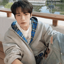 a young man wearing a plaid jacket and a necklace