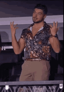 a man wearing a floral shirt and khaki pants is making a peace sign