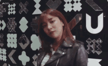 a woman in a leather jacket stands in front of a wall with the letter u visible