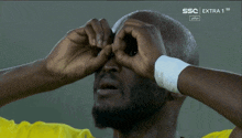 a man covering his eyes in front of a screen that says extra 1