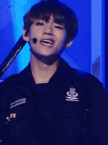 a young man is wearing a black jacket and holding a microphone while singing into it .