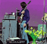 a man is playing a guitar on stage with a vase of flowers in front of him