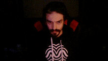 a man with a beard is wearing a black shirt with a white spider on it