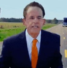 a man in a suit and orange tie is standing on the side of a highway .