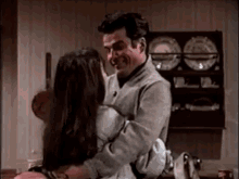 a man is holding a woman in his arms and they are hugging each other in a kitchen .